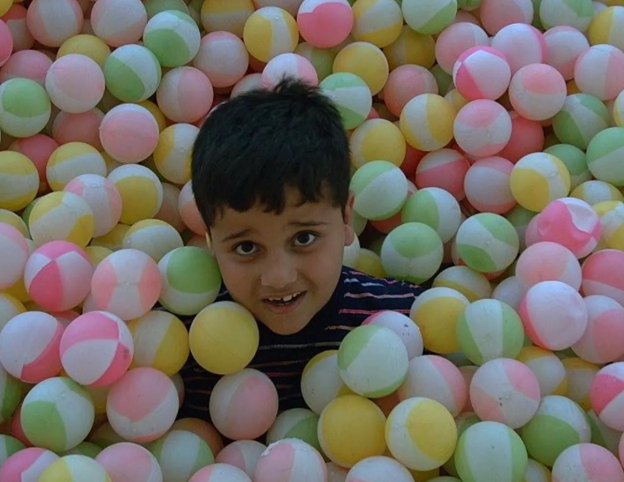 mehrad as a small boy, up to the chin in a ball pit of pastel balls