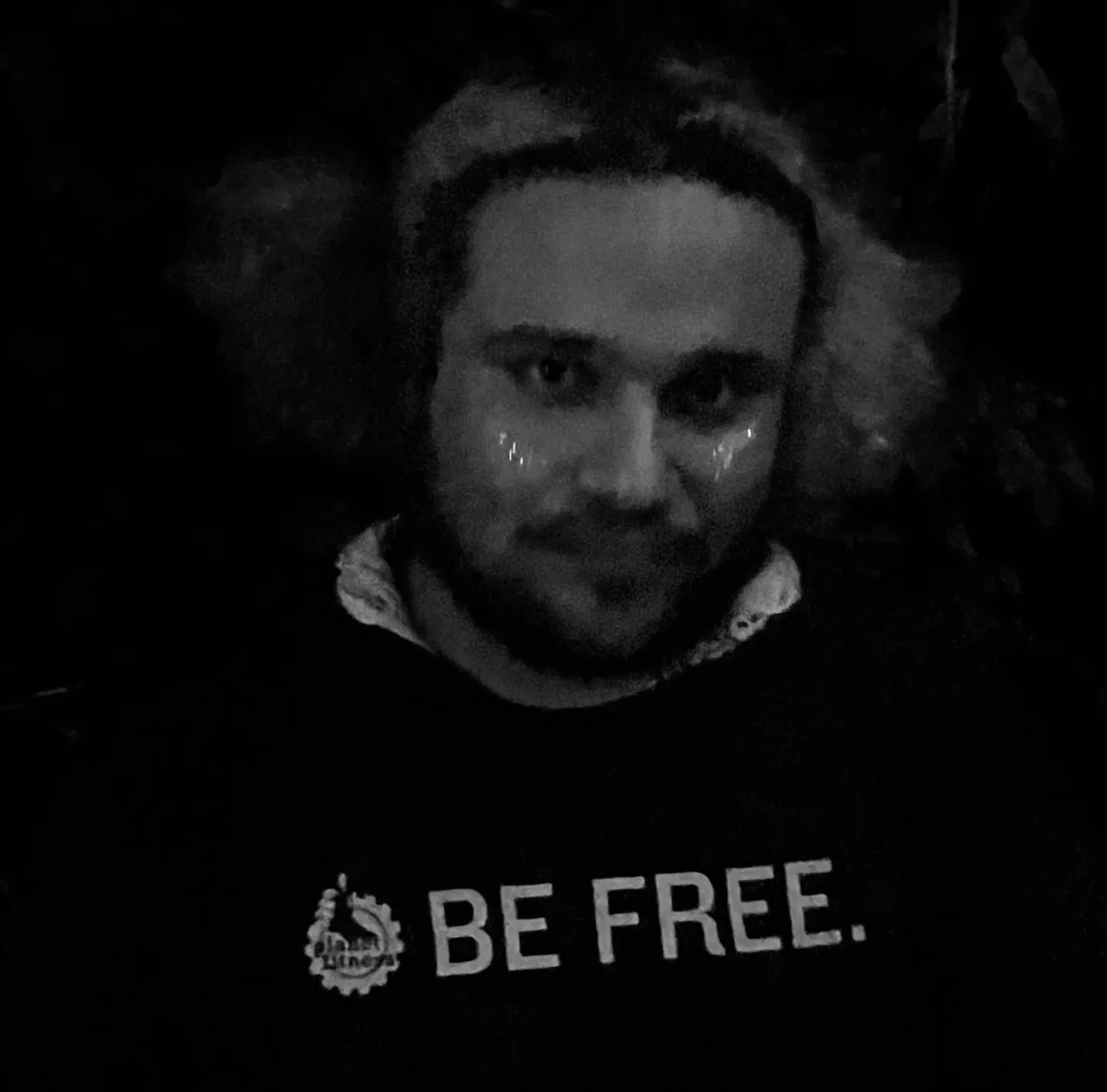 mehrad at night in black and white, glitter on the cheeks, a t-shirt that says be free