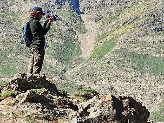 mehrad on a rock high in the mountains, a backpack on, taking a photo